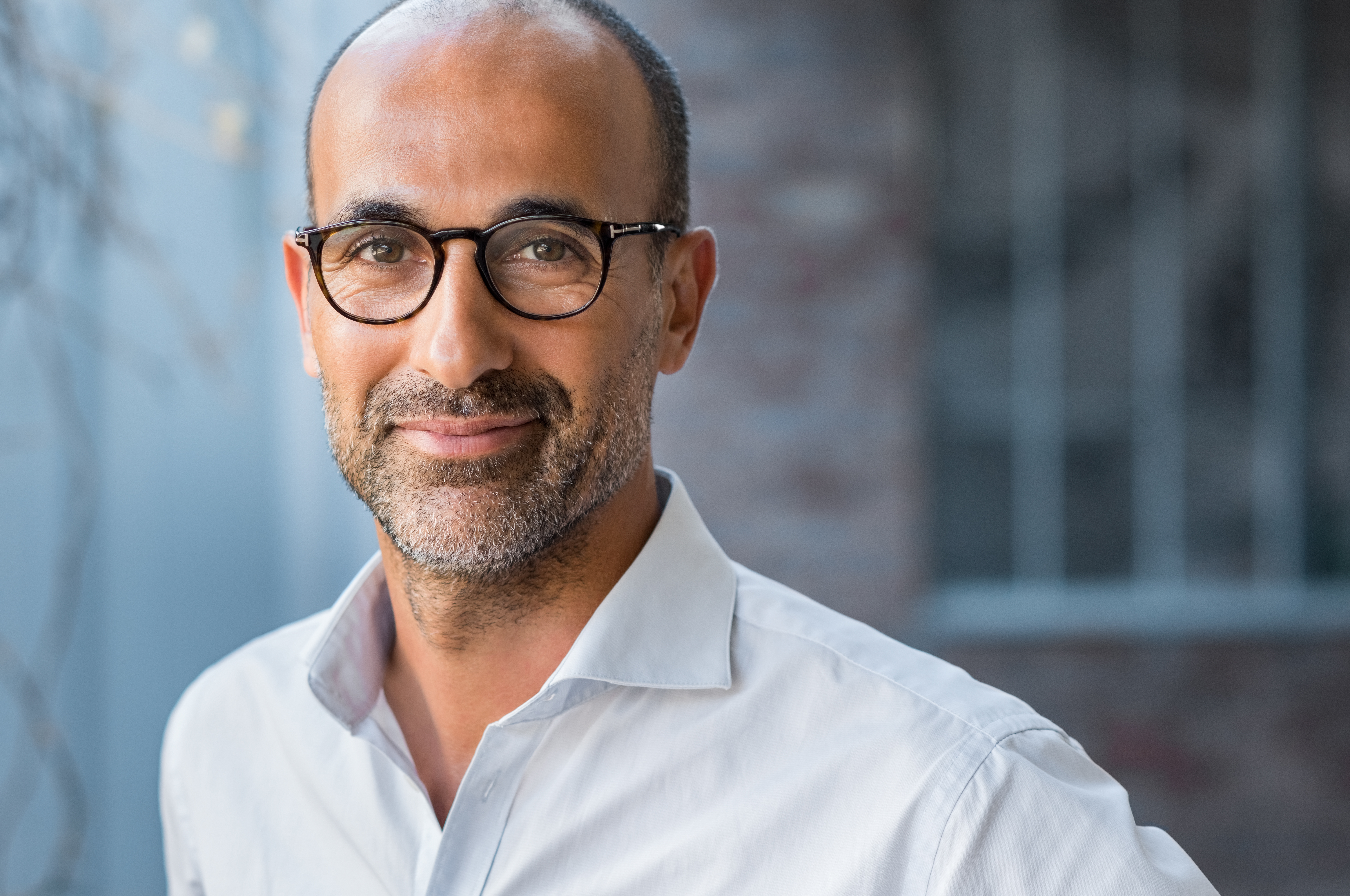 Portrait of happy mature man wearing spectacles and looking at camera outdoor. Man with beard and glasses feeling confident. Close up face of hispanic business man smiling.